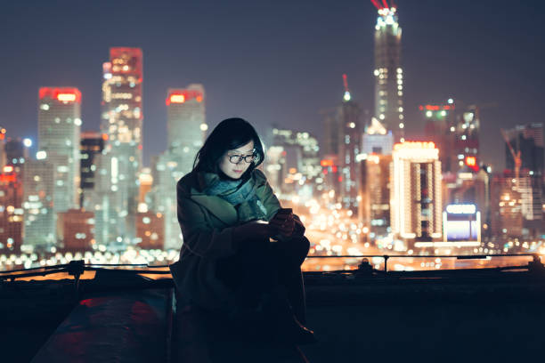 frau mit smartphone steht auf wolkenkratzer-dach - night beijing city asia stock-fotos und bilder