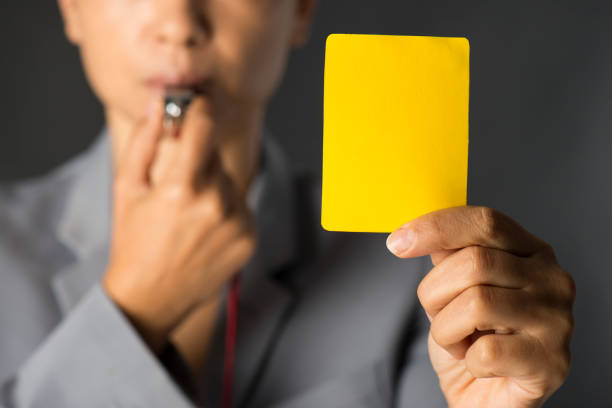 mujer de negocios sosteniendo la tarjeta amarilla y que sopla un silbato - silbar fotografías e imágenes de stock