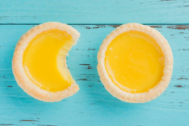 sesión de estudio vista superior de huevo dos tartas con una mordida y completa sobre un fondo de madera - egg tart fotografías e imágenes de stock