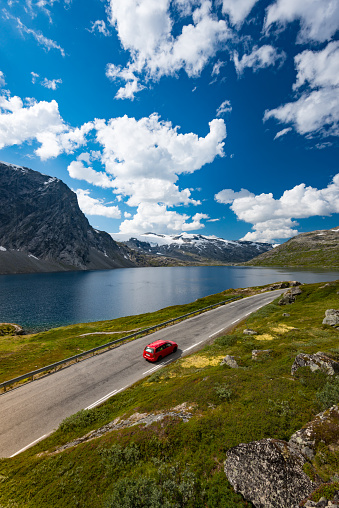 Red car in mountains of Norway, Europe. Auto travel through scandinavia. Blue cloudy sky and lake in background.