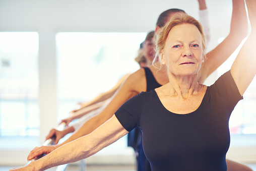 Smiling aged woman looking at camera while dancing ballet with group in the class.