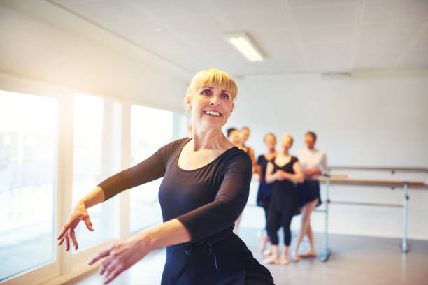 Smiling mature woman ballet dancing in a studio Smiling senior woman practicing ballet in a dance studio with a group of friends in the background dance studio instructor stock pictures, royalty-free photos & images