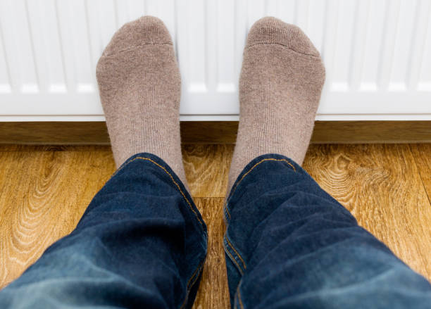 istock Person in winter socks warming cold feet in front of heating radiator. 876601092