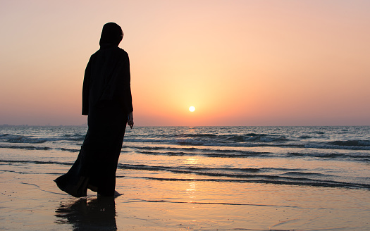 Woman in hijab standing on the beach looking at horizon