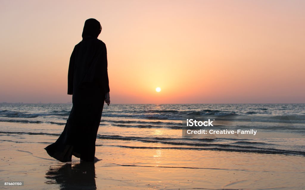 Woman in hijab standing on the beach Woman in hijab standing on the beach looking at horizon Women Stock Photo