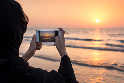 Woman in hijab taking picture of a sunset on the beach