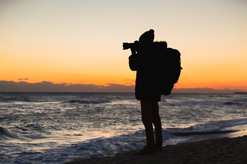 A traveler with a backpack is standing on the seashore and photographing the sunrise on Japan Sea, South Korea
