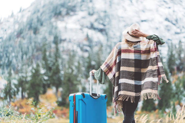istock Traveling woman with bright blue suitcase looking at mountain wilderness 876616414