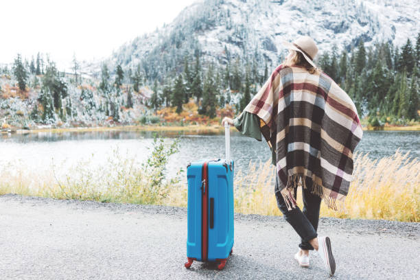 istock Traveling woman with bright blue suitcase looking at mountain wilderness 876621602