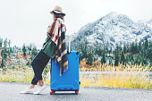 Traveling woman sitting on her blue suitcase next to wild landscape