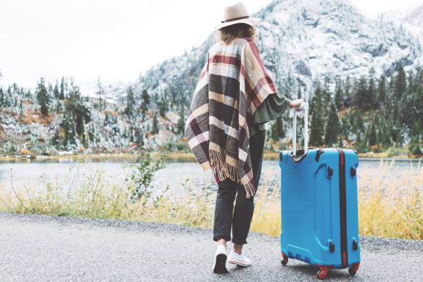istock Traveling woman with bright blue suitcase looking at mountain wilderness 876625332