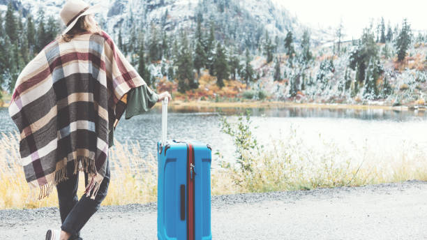 istock Traveling woman with bright blue suitcase looking at mountain wilderness 876625462