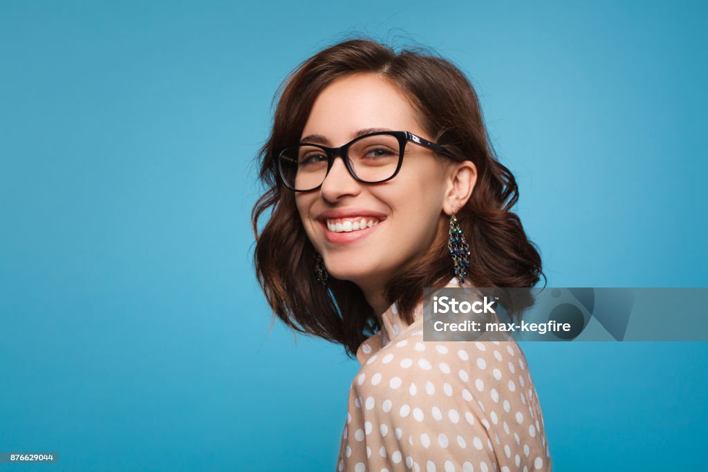 Smiling woman posing in glasses Elegant cheerful brunette in eyeglasses smiling at camera on blue background. Eyeglasses Stock Photo