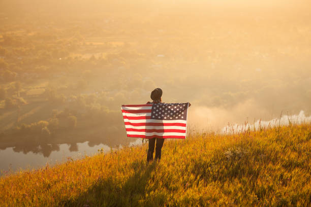 Back view of anonymous male traveler posing with American flag on background of countryside.