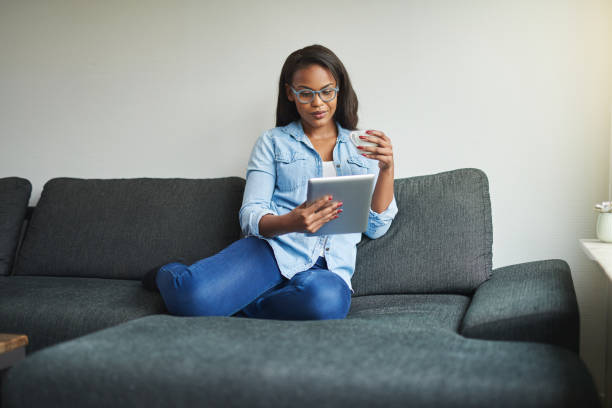 istock Smiling woman drinking coffee and using a tablet at home 876632696