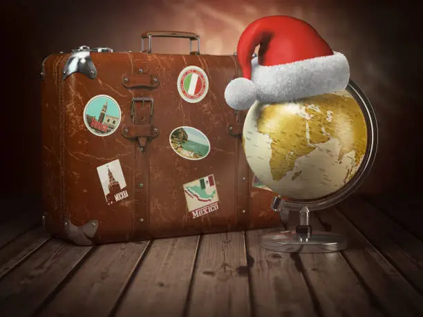 Photo of Christmas or new year travel concept. Old suitcase with globe nad santa hat on wood  background.