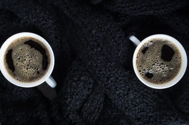 Top view of a small white cups of coffee on a background of black wool scarf with shallow depth of focus