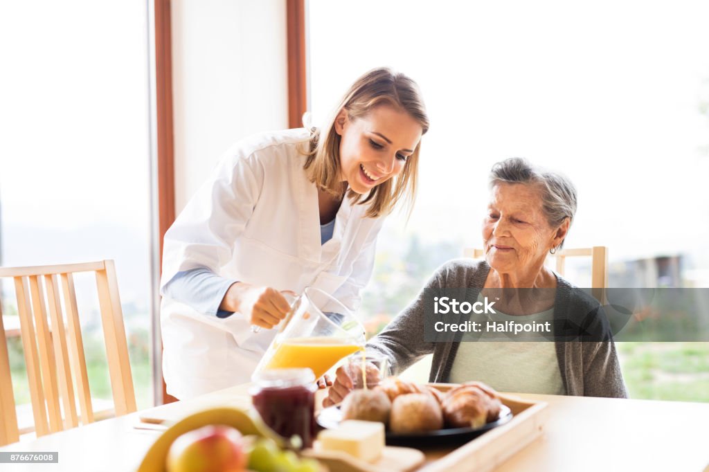 Health visitor and a senior woman during home visit. Health visitor and a senior woman during home visit. A nurse pouring orange juice to an elderly woman. Food Stock Photo