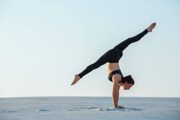 istock Young woman practicing inversion balancing yoga pose handstand on sand 876708926
