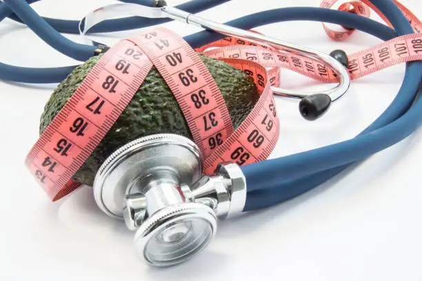 Use avocado in weight loss under medical supervision of nutritionist. Stethoscope listening ripe avocado fruit, which wrapped up measuring tape. Avocados as healthy food that helps in losing weight
