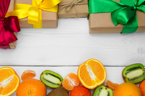 Fruit orange, tangerine and kiwifruit and gift box with ribbon bow on white wooden retro background