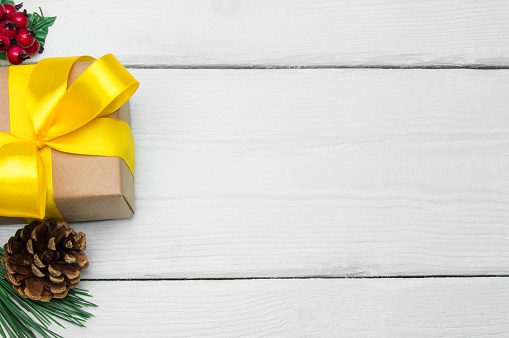 Gift box with yellow ribbon bow and branch christmas tree with cone on white wooden vintage background