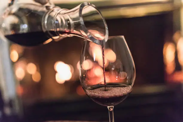 Photo of Unrecognizable woman, a decanter in her hands, pouring red wine in a glass.