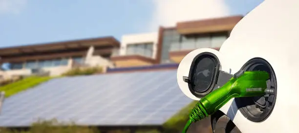 Close up view of Electric Car charging and houses with solar panels in the background