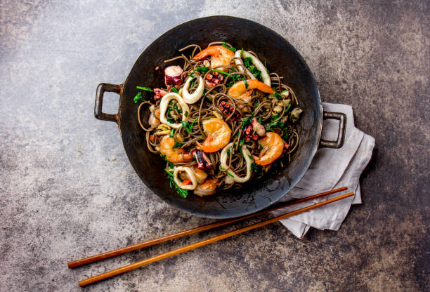 salteado de alforfón tallarines con mariscos - camarones, pulpo, calamar en hierro fundido asiática wok con palillos de cocina. vista superior, fondo de piedra - asian cuisine fotografías e imágenes de stock