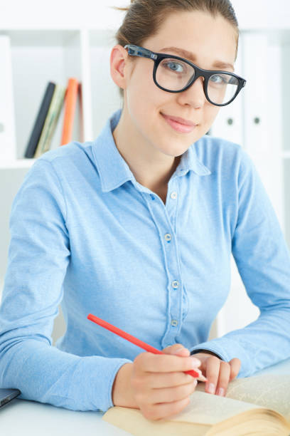 istock Female student at workplace with book holding red pencil studying. 876774544