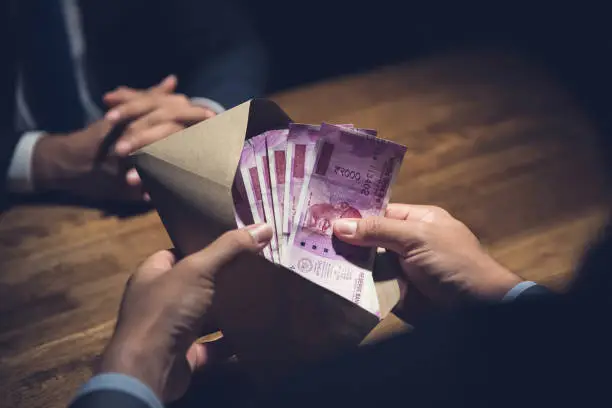 Photo of Businessman counting money, Indian Rupee currency, in the envelope just given by his partner after making an agreement in private dark room