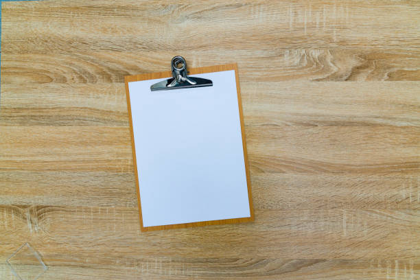 istock clipboard with blank white paper sheet on wood table top view with copy space. 876774782