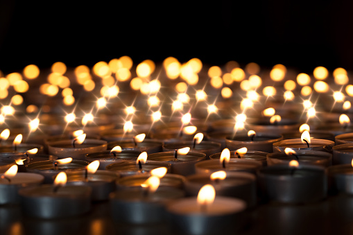 Tealight candles. Beautiful Christmas celebration, religious, or remembrance candlelight image. Romantic candlelit vigil. Selective focus against black background.