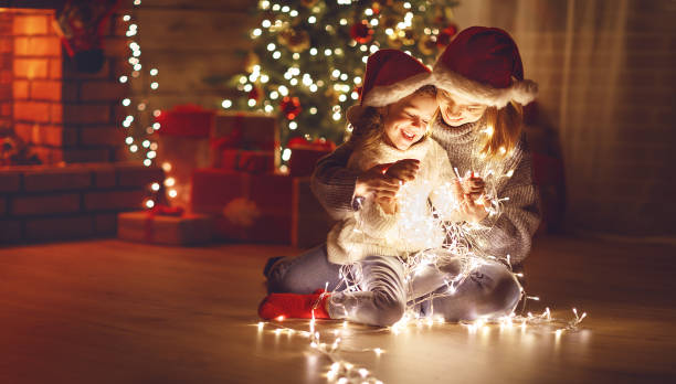 frohe weihnachten! mutter und kind tochter mit glühenden girlande in der nähe von baum - christmas family child christmas tree stock-fotos und bilder