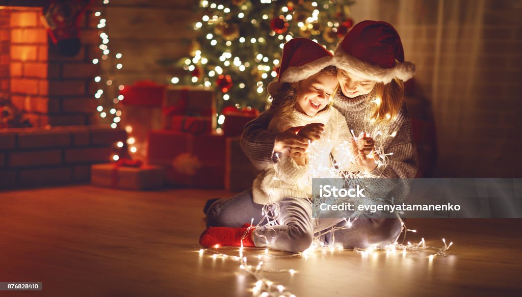 Merry Christmas! mother and child daughter with glowing garland near tree Merry Christmas! mother and child daughter with a glowing Christmas garland near tree Christmas Stock Photo