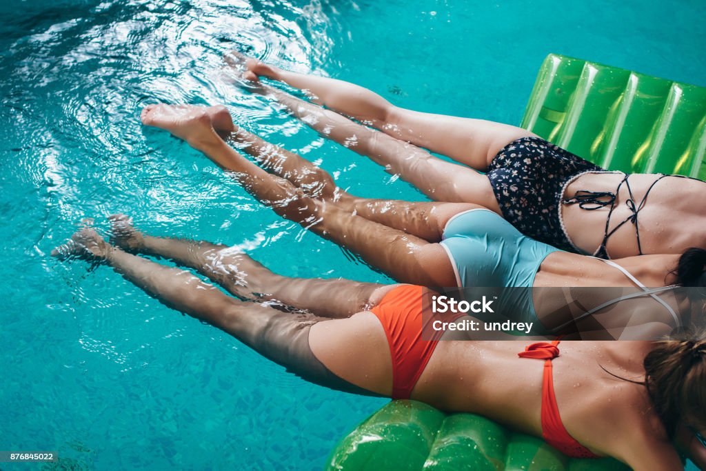 Three slim girlfriends wearing swimsuits lying on air mattress swimming in the swimming pool Three slim girlfriends wearing swimsuits lying on air mattress swimming in the swimming pool. Swimming Pool Stock Photo