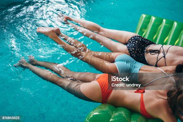 Three Slim Girlfriends Wearing Swimsuits Lying On Air Mattress Swimming In The Swimming Pool Stock Photo - Download Image Now