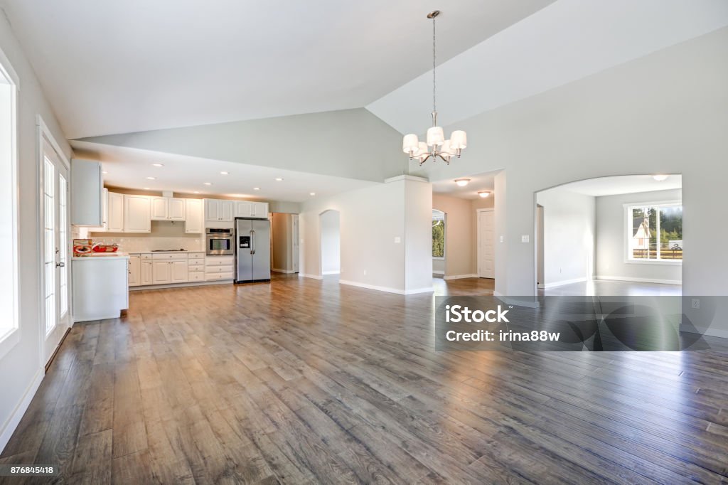 Spacious rambler home interior with vaulted ceiling Spacious rambler home interior with vaulted ceiling over glossy laminate floor. Empty light filled dining or living space adjacent to new white kitchen room features pale grey walls. Northwest, USA Wood Laminate Flooring Stock Photo