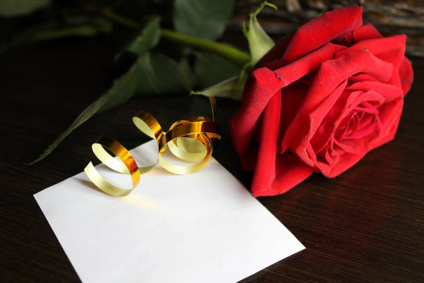 Pink envelope, pink roses and golden ribbon on black table.