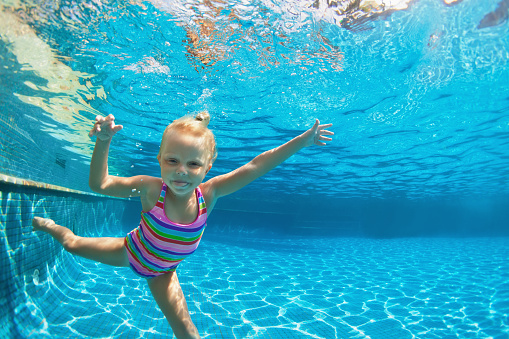 Funny portrait of child learn swimming, diving in blue pool with fun - jumping deep down underwater with splashes. Healthy family lifestyle, kids water sports activity, swimming lesson with parents.
