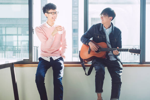istock Man playing guitar while friend sitting with drinking water at home 876861884