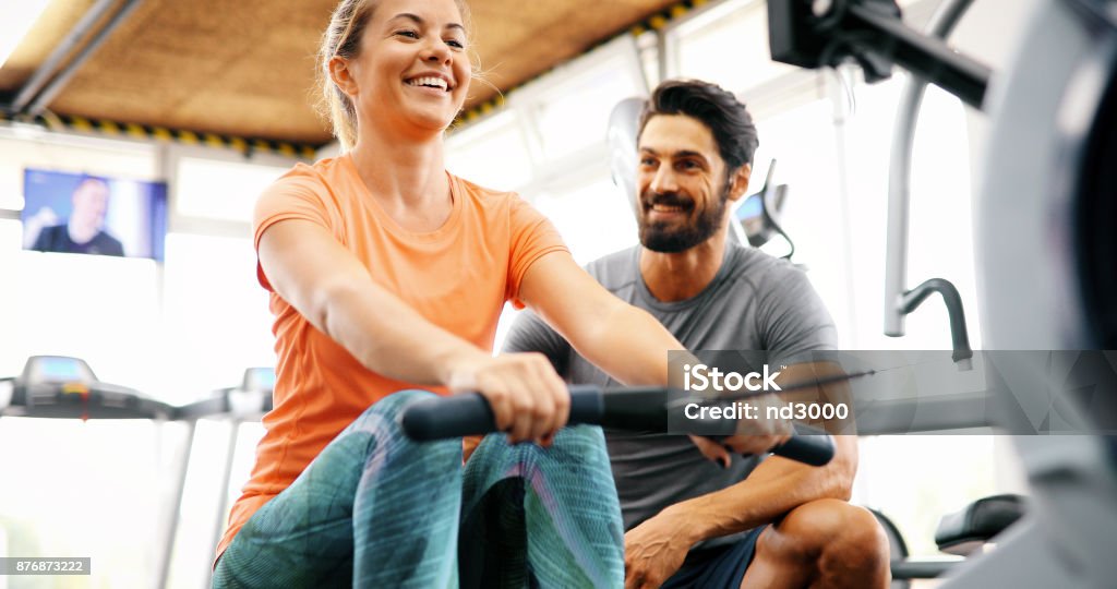 Hermosa joven haciendo ejercicios con entrenador personal - Foto de stock de Máquina de remo libre de derechos