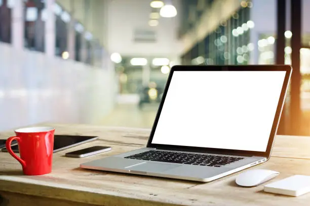 Photo of Laptop with blank white screen on table in office background