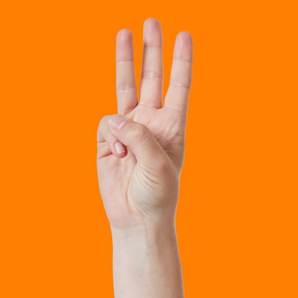 istock Hand with three raised fingers counts '3' against orange background 876885340