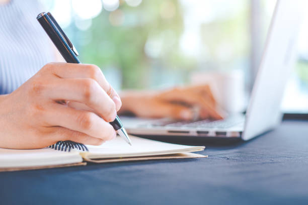 istock Woman hand writing on notepad with a pen and works in a laptop computer in the office. 876890168