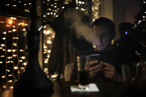 Photo of man holding hookah pipe and smoking in a night club