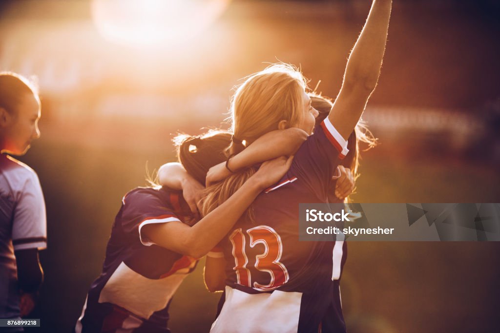 Celebrating the victory after soccer match! Team of happy female soccer players celebrating their achievement on a playing field at sunset. Sport Stock Photo