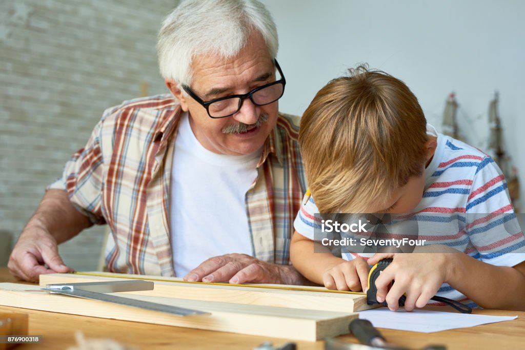 Grandfather Teaching Boy Carpentry Portrait of old man teaching cute little boy woodwork, making wooden models together working at desk in small studio Grandfather Stock Photo