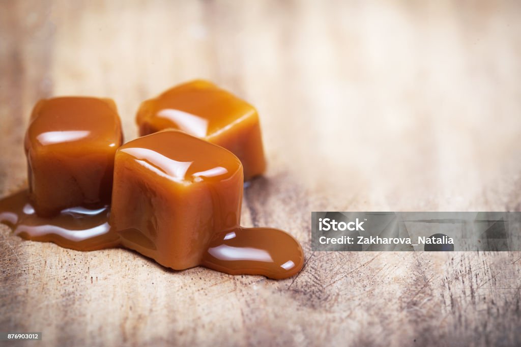 Zelfgemaakte karamelsaus stroomt op caramel snoepjes op houten achtergrond. - Royalty-free Karamel Stockfoto