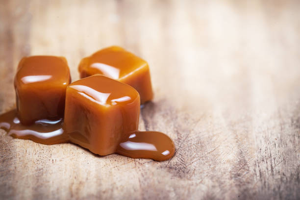 Homemade  Caramel sauce flowing on caramel candies on wooden  background. Homemade  Caramel sauce flowing on caramel candies on wooden  background. fudge stock pictures, royalty-free photos & images